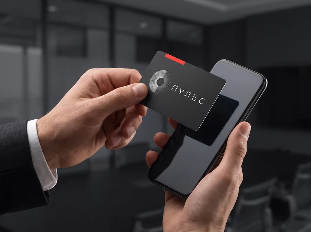 Чёрную NFC-визитку с логотипом ПУЛЬС подносят к смартфону